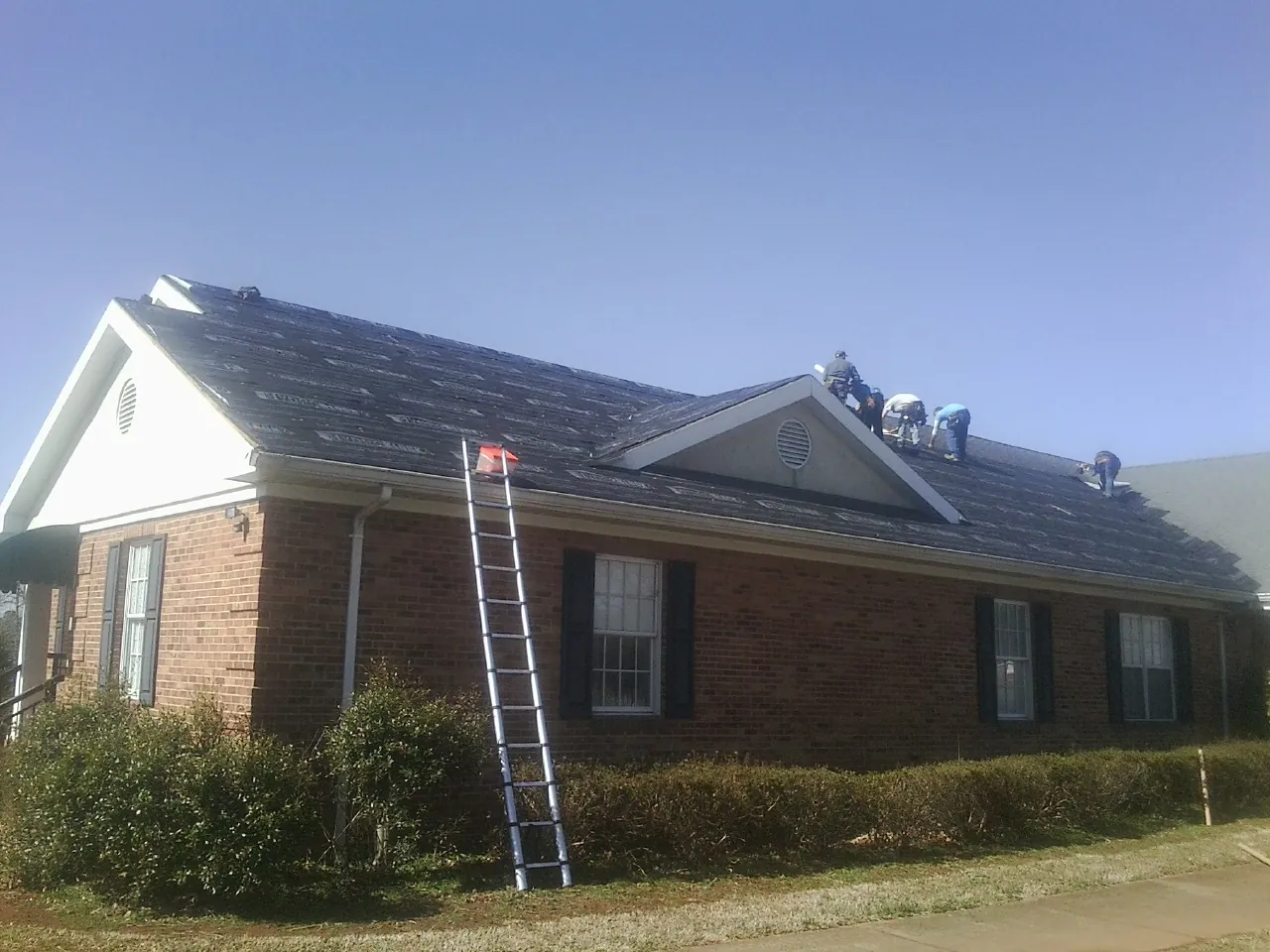 Crew tearing shingles off a brick ranch roof with a ladder set — Metal Roof Repair work by our crew in Bouckville