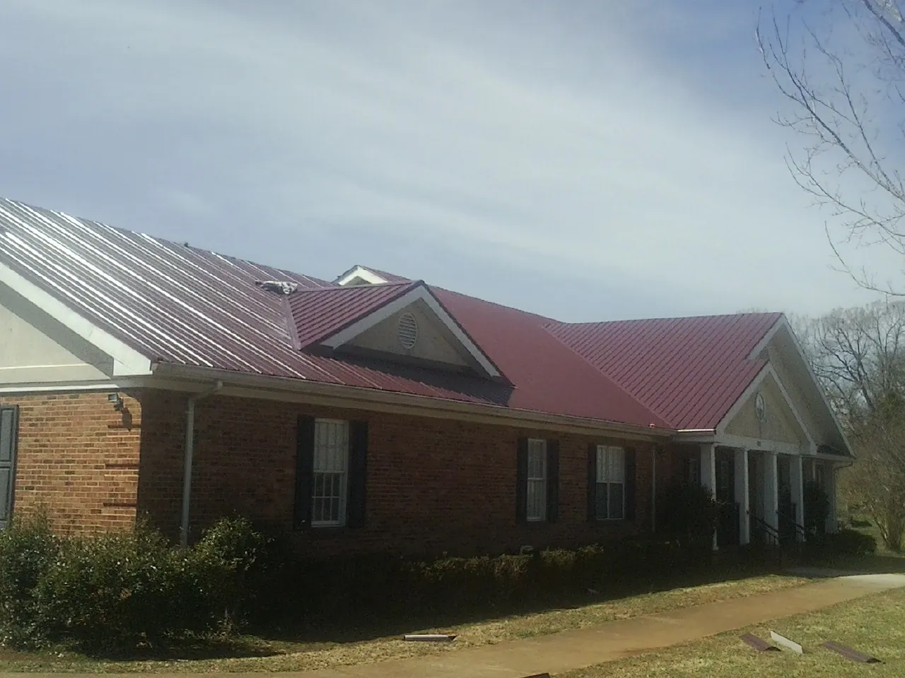 Red metal roof with gabled entries on a long brick building, from a Hail Damage Roof Repair job in Bouckville