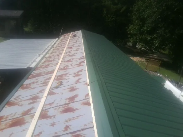 Old rusted panels beside newly installed green metal roofing — Wind Damage Roof Repair by Roofing Brothers in Bouckville