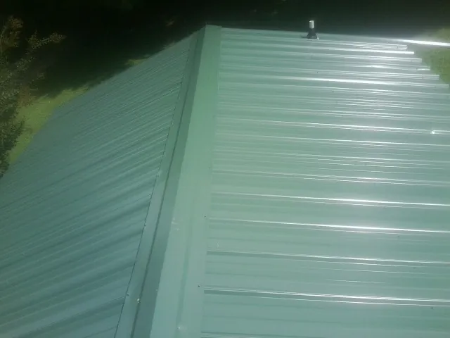 New green metal panels meeting at the ridge of a roof — Flat Roof Repair work by our crew in Bouckville