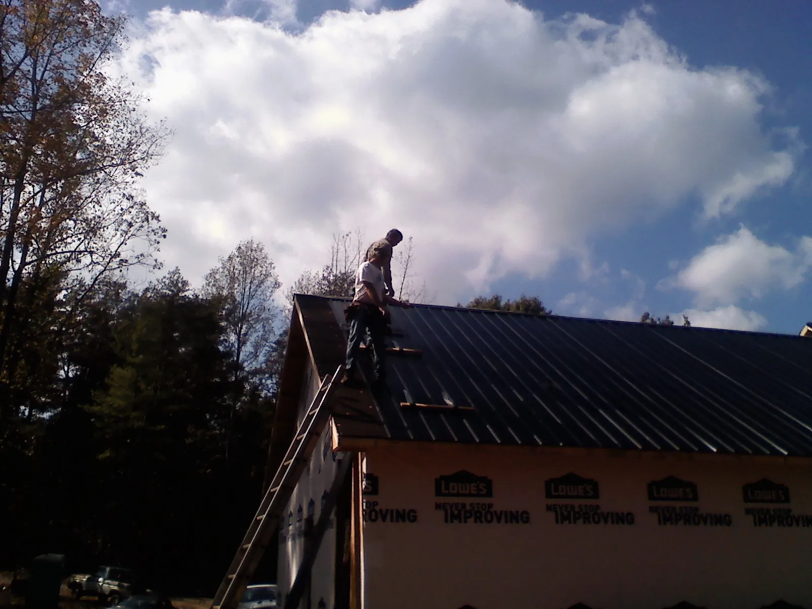 Roofer fastening dark metal panels high against a cloudy sky, from a Roof Inspection job in Bouckville