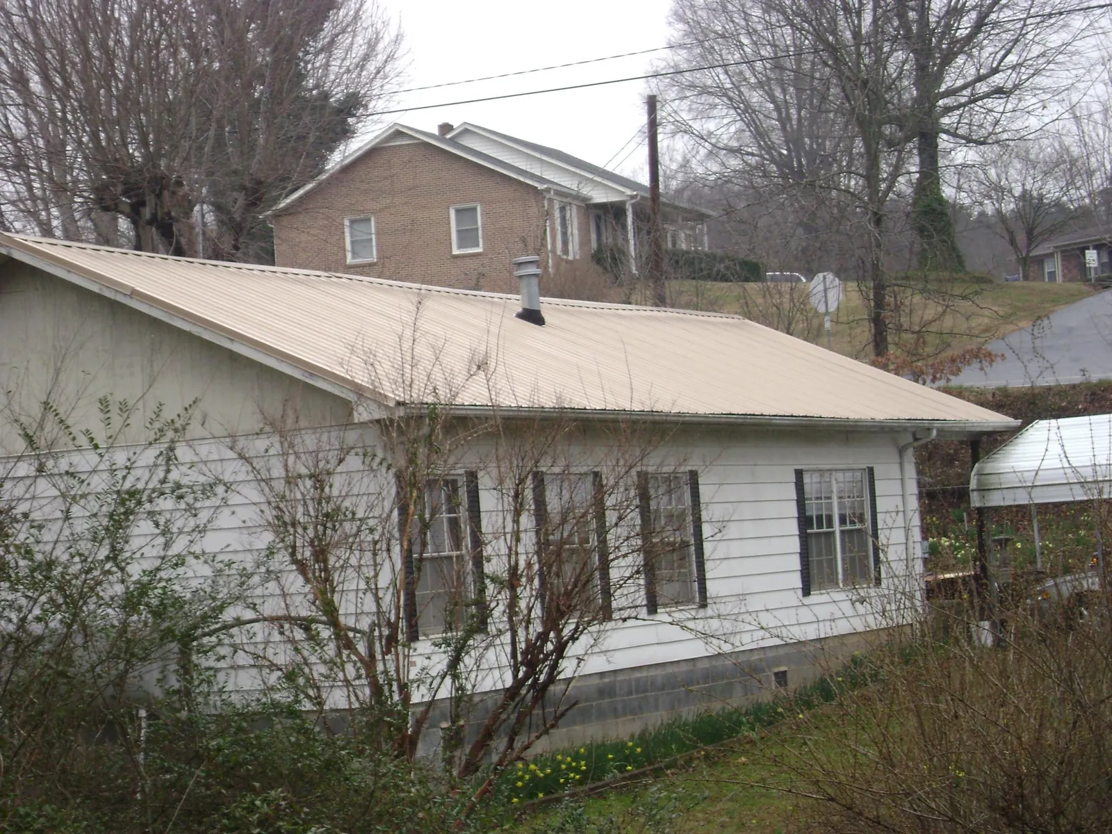 Tan metal roof on a white sided house set into a hillside — Commercial Roofing by Roofing Brothers in Bouckville