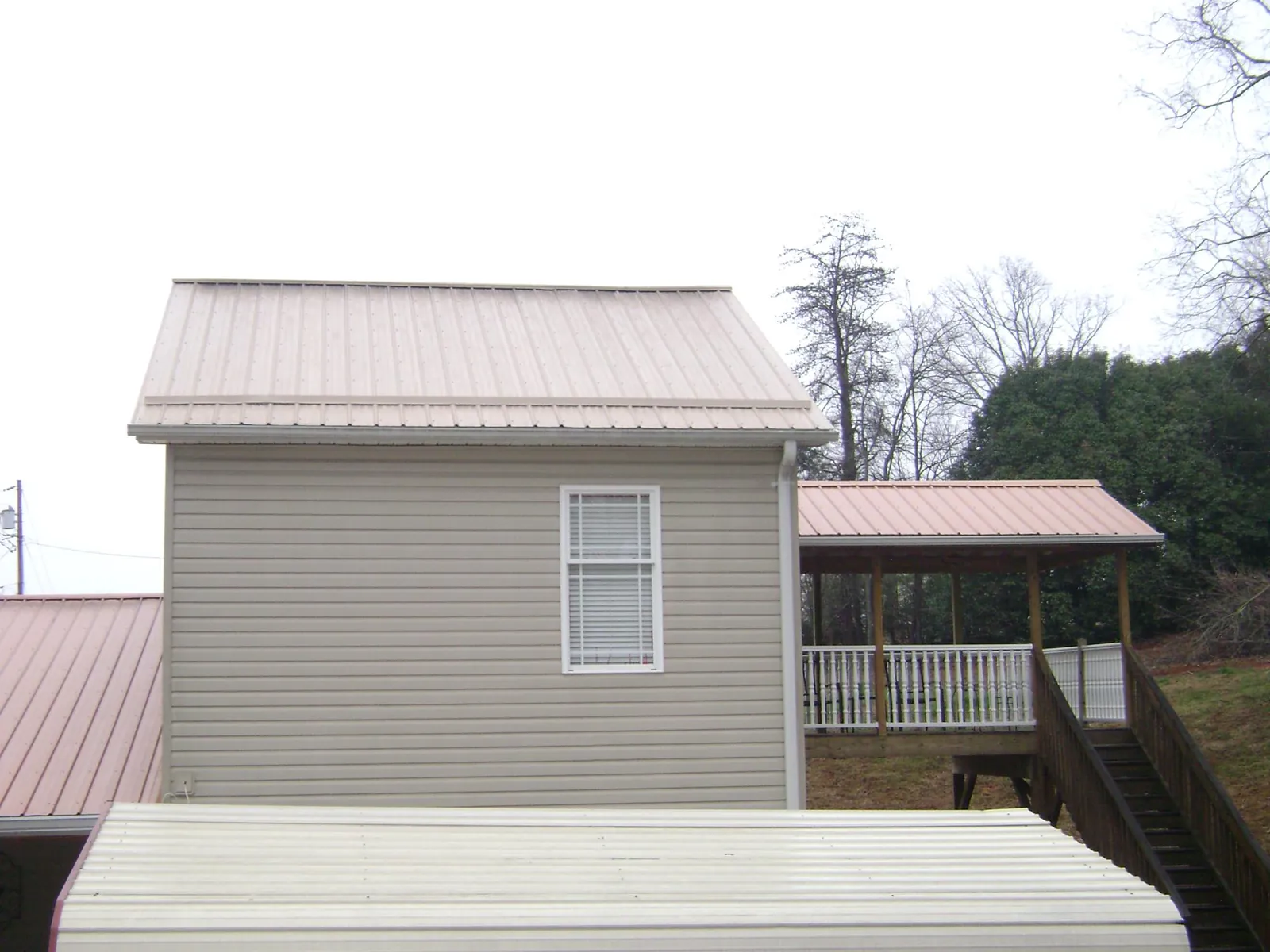 Tan metal roofs on a two story addition and attached porch, from a Roof Replacement job in Bouckville